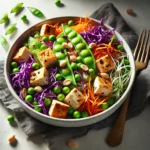 Colorful tofu salad with tofu cubes, shredded purple cabbage, snow peas, grated carrots, green peas, and a sprinkle of peanuts, served in a white bowl on a dark cloth napkin with a fork beside it.