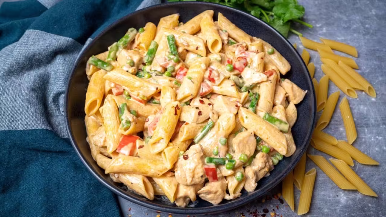 A bowl of spicy chicken chipotle pasta garnished with fresh herbs and a lime wedge